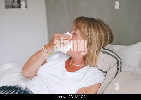 Femme sénior malade soufflant le nez tout en étant couché sur le lit à accueil Banque D'Images