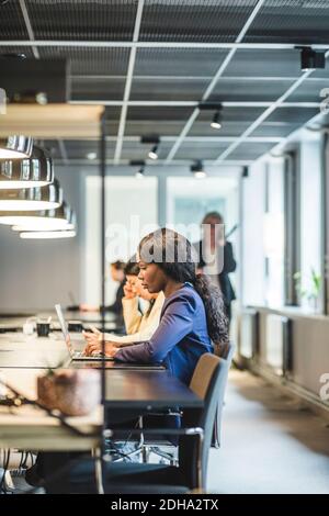 Femme d'affaires travaillant sur un ordinateur portable tout en étant assise avec un collègue au bureau Banque D'Images