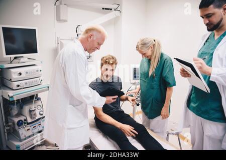 Médecin mature montrant une tablette numérique à un jeune patient de sexe masculin lit par des collègues à l'hôpital Banque D'Images