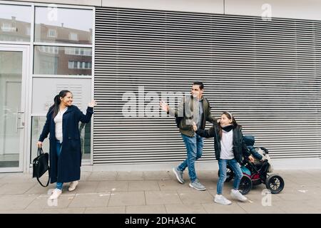 Père et fille qui agite à mère tout en marchant sur le trottoir avec poussette en ville Banque D'Images