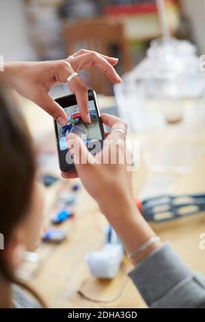 Image rognée d'une jeune femme technicien touchant l'écran mobile pendant photographier le modèle sur la table en atelier Banque D'Images