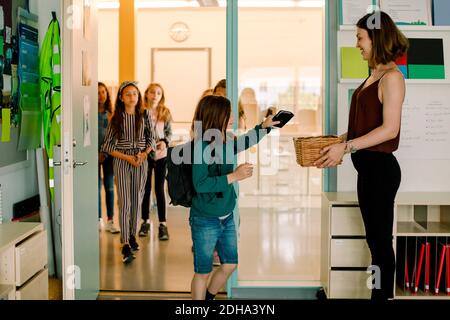 Fille gardant le téléphone dans le panier tout en souriant femme enseignant à la recherche à l'étudiant en classe Banque D'Images