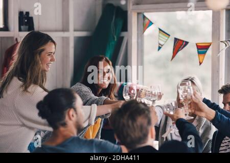 De jeunes amis toaster des lunettes de vin tout en étant assis à la maison Banque D'Images