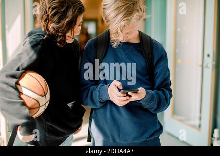 Des élèves de sexe masculin utilisent un smartphone dans le couloir scolaire Banque D'Images