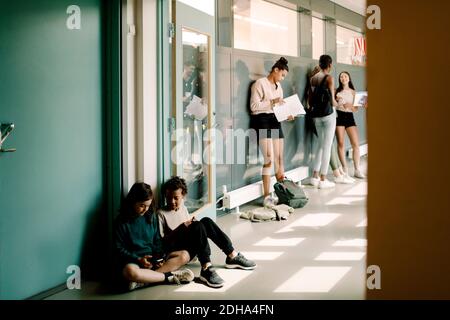 Garçon et fille assis à la porte pendant que les élèves de niveau élevé junior parler dans le couloir de l'école