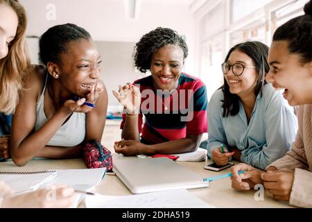 Un professeur souriant se fait le gai pendant que des étudiants sont assis à table salle de classe Banque D'Images