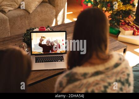 Vue arrière de la femme et du fils ayant un vidéocall avec couple en chapeau de père noël en grillage sur ordinateur portable à la maison Banque D'Images