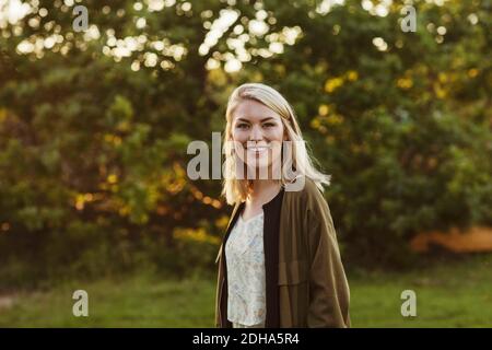 Portrait d'une jeune femme blonde souriante debout contre les arbres Banque D'Images