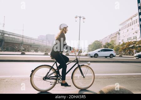 Longueur totale de la femme de direction portant un casque à vélo route en ville Banque D'Images