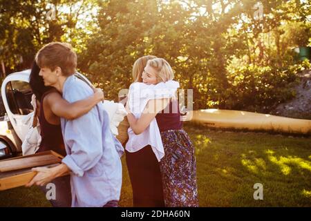 Des amis hommes et femmes heureux s'embrassant tout en se tenant contre les arbres au jardin Banque D'Images