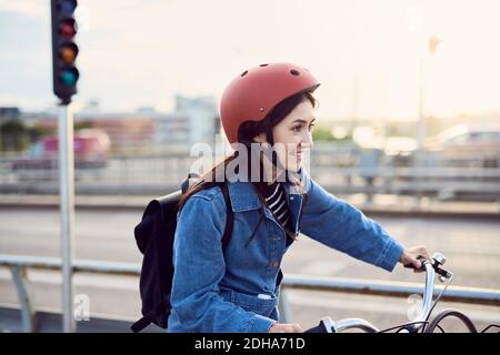Femme de taille moyenne souriante à vélo en ville Banque D'Images
