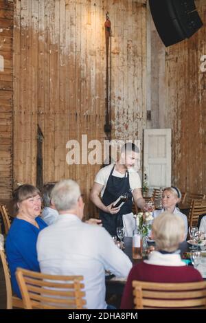 Jeune serveur servant du vin à des amis seniors à table restaurant Banque D'Images