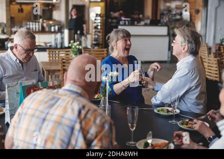 Couple senior qui toaste des flûtes tout en déjeunant avec des amis restaurant Banque D'Images