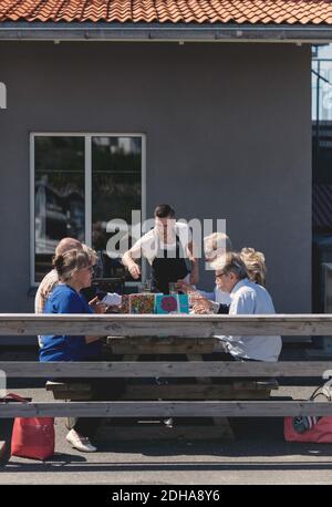 Un jeune serveur sert de la nourriture à des amis seniors à l'extérieur du restaurant Banque D'Images