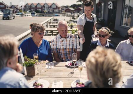 Un jeune serveur sert de la nourriture à des amis seniors à table patio du restaurant Banque D'Images