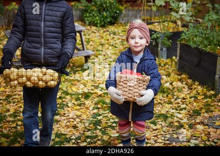 Portrait d'une fille souriante avec panier de légumes tout en restant debout un frère masculin dans la cour arrière Banque D'Images