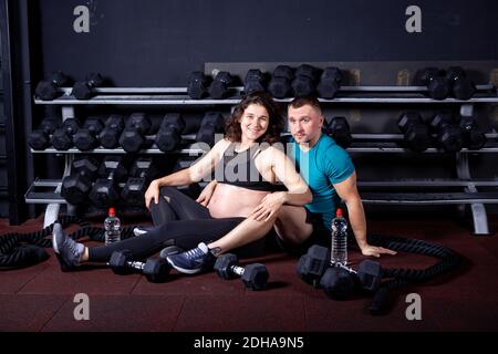 Sport de grossesse en famille dans la salle de sport urbaine de cross-training. Le sport et un mode de vie sain pendant la grossesse. Jeune couple qui s'embrasse sur la salle de sport fl Banque D'Images