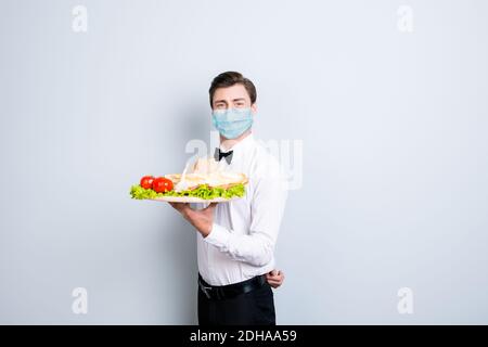 Portrait d'un homme de classe qui porte un masque de gaze de sécurité sur le plateau repas délicieux servant isolé sur fond gris Banque D'Images