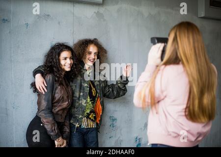 Vue arrière d'une jeune fille qui photographie des amis adolescents souriants debout contre mur au garage Banque D'Images