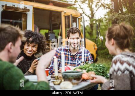 Des amis heureux s'amusant en parlant à table pendant le camping Banque D'Images