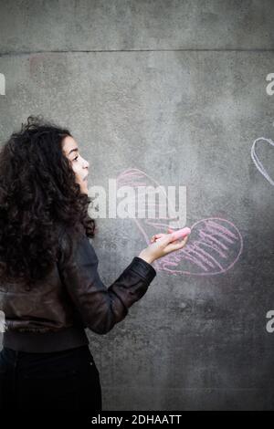 Vue arrière d'une adolescente en forme de coeur sur le mur avec de la craie rose Banque D'Images