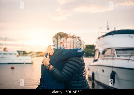 Vue latérale de l'homme et de la femme âgés qui s'embrassent au port au coucher du soleil Banque D'Images