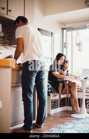 Mère et fille utilisant un ordinateur portable pendant que le père travaille dans la maison cuisine Banque D'Images