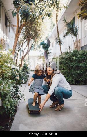 Elle fait du skateboard avec l'aide de sa mère sur la piste de marche Banque D'Images