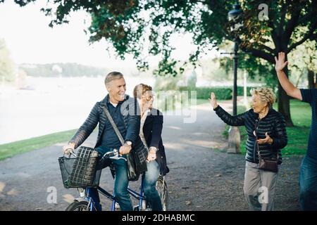 Couple senior qui agite des amis en vélo tandem dans le parc Banque D'Images