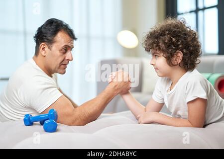 Adorable petit garçon latin et son père s'amusant ensemble à la maison tout en luttant sur le canapé. Mode de vie sain, concept de famille. Vue latérale Banque D'Images