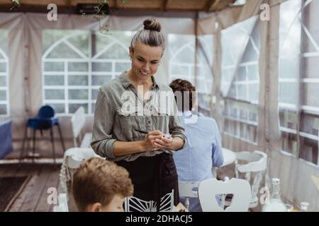 Femme propriétaire prenant la commande du client pendant qu'elle est assise au restaurant Banque D'Images