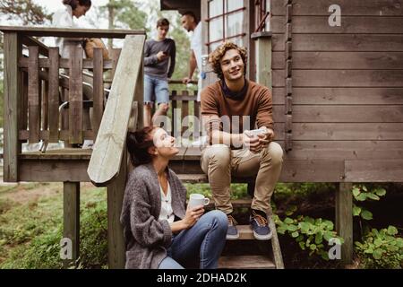 Femme souriante regardant un homme assis sur des marches pendant que des amis debout en arrière-plan Banque D'Images