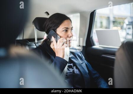 Femme d'affaires parlant au téléphone en étant assise dans la voiture Banque D'Images