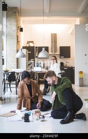 Des architectes souriants travaillent tandis que des femmes entrepreneurs sont assises en arrière-plan à bureau à domicile Banque D'Images