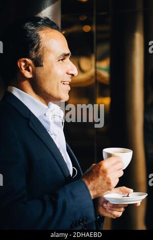 Vue latérale d'un homme d'affaires mûr souriant tenant une tasse de café vue sur le café Banque D'Images