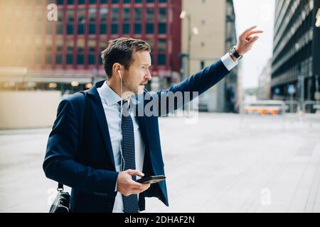 Homme d'affaires mature tenant un téléphone portable tout en hélant un taxi dans la ville Banque D'Images