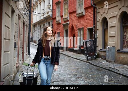 Jeune femme regardant loin en marchant avec des bagages dans une allée Banque D'Images