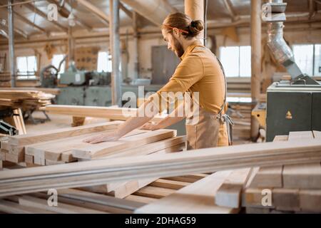 Charpentier choisissant des planches de pin dans un entrepôt d'atelier de menuiserie. Préparation des matières premières pour le travail du bois futur Banque D'Images