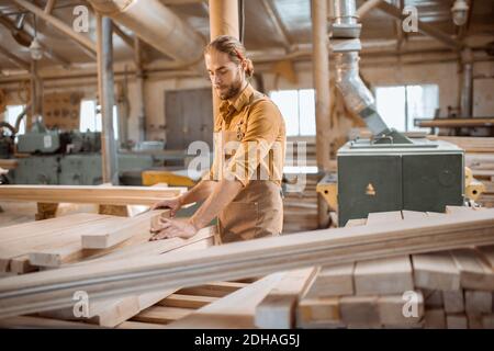 Charpentier choisissant des planches de pin dans un entrepôt d'atelier de menuiserie. Préparation des matières premières pour le travail du bois futur Banque D'Images