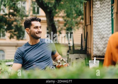 Jeune homme souriant assis avec un ami au restaurant de la ville Banque D'Images