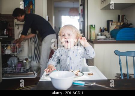 Pleurs hommes tout-petits regardant loin en étant assis sur une chaise haute dans la cuisine de l'appartement Banque D'Images