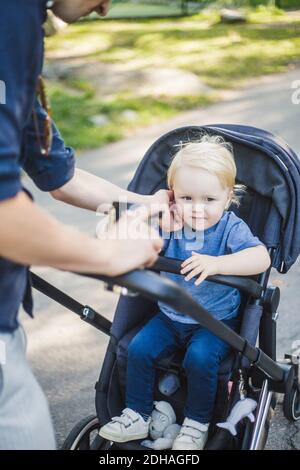 Section médiane de l'homme touchant son fils assis sur le chariot de bébé à parc public Banque D'Images