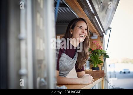 Jeune femme souriante regardant loin en se tenant dans un camion de nourriture en ville Banque D'Images