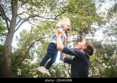 Vue en contre-plongée d'un homme souriant qui attrape un bébé blond contre les arbres Banque D'Images