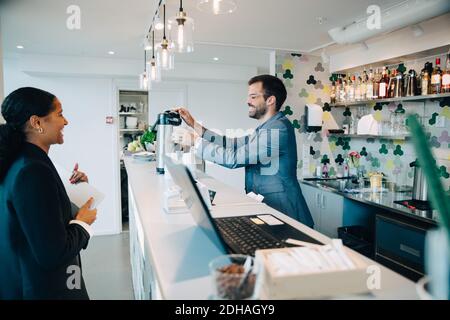 Le propriétaire souriant prépare un café pour une femme à la cafétéria du bureau Banque D'Images