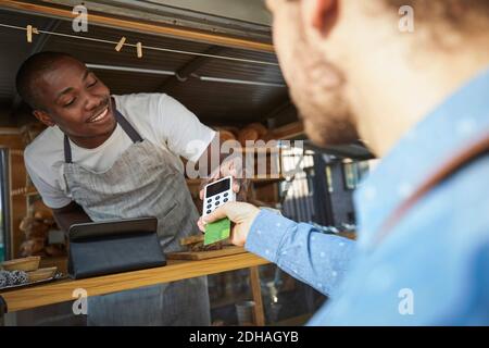 Homme avec un vendeur payant par carte de crédit au camion alimentaire Banque D'Images