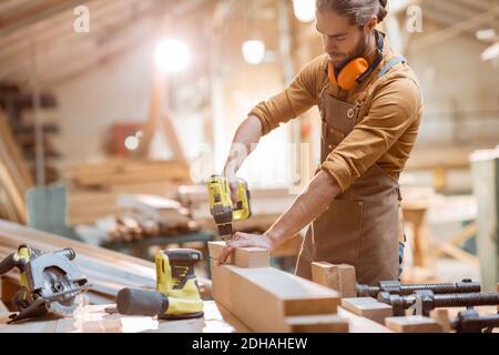 Menuisier travaillant avec des outils sans fil modernes et des barres en bois l'atelier à l'atelier Banque D'Images