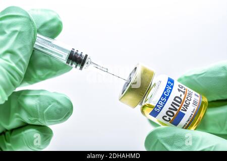 Hände in Zutzhandschuhen halten Injektionsfläschchen mit Corona-Impfstoff und Impfspritze, Symbolfoto Corona-Impfmittel