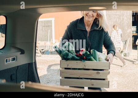 Femme mûre en train de charger une caisse pleine de légumes biologiques dans la voiture coffre Banque D'Images