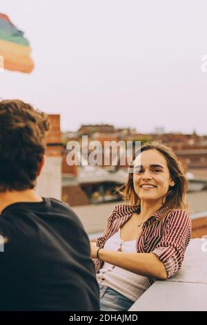 Portrait de la femme heureuse assise avec un ami sur la terrasse contre ciel Banque D'Images